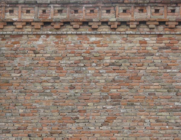 Brick fence texture made up of eroded red and grey bricks, with large mortar gaps in between them. A row of uniformly patterned bricks line the top.